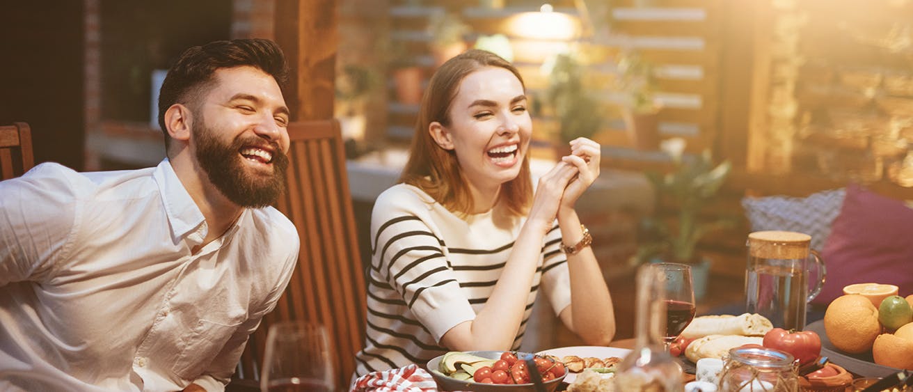 A young man and a young woman laughing while eating a beautiful dinner.